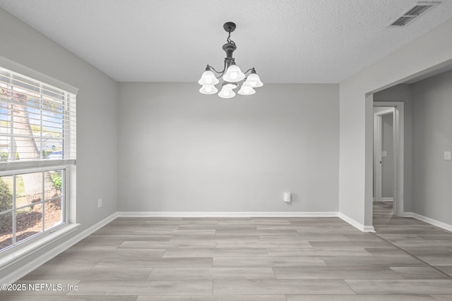 empty room with baseboards, visible vents, a textured ceiling, light wood-type flooring, and a notable chandelier