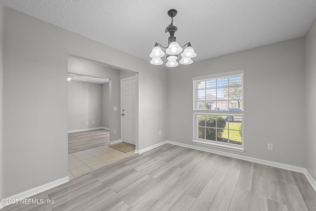 spare room with baseboards, a textured ceiling, light wood-type flooring, and an inviting chandelier