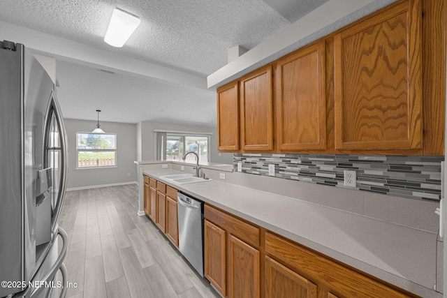 kitchen with stainless steel appliances, light countertops, decorative backsplash, brown cabinetry, and a sink