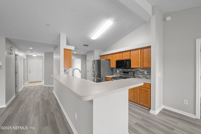 kitchen with tasteful backsplash, light countertops, appliances with stainless steel finishes, brown cabinetry, and light wood-style floors