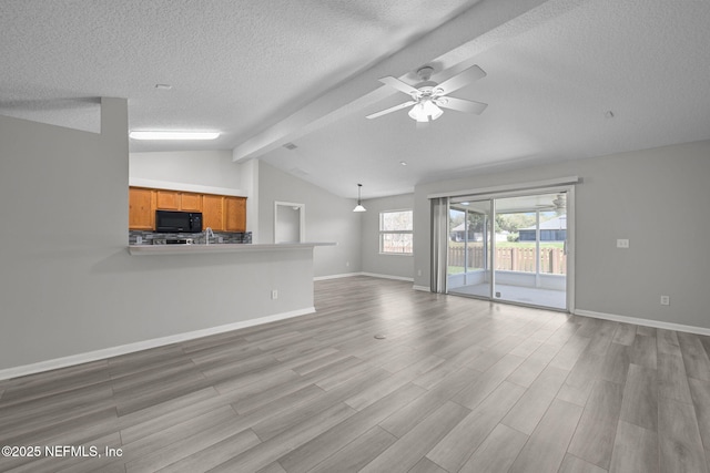 unfurnished living room with light wood finished floors, lofted ceiling with beams, ceiling fan, a textured ceiling, and baseboards