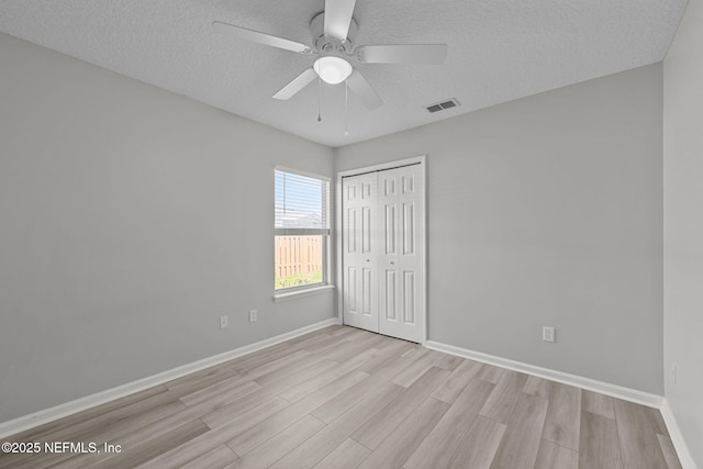 unfurnished bedroom with baseboards, visible vents, a textured ceiling, light wood-style floors, and a closet