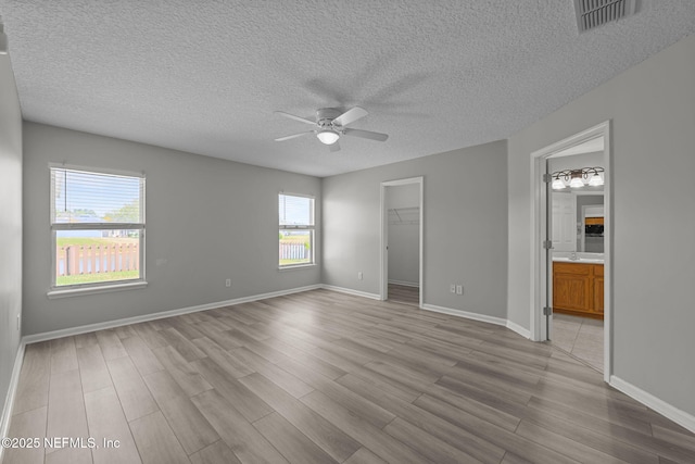 unfurnished bedroom with ensuite bathroom, wood finished floors, visible vents, baseboards, and a spacious closet