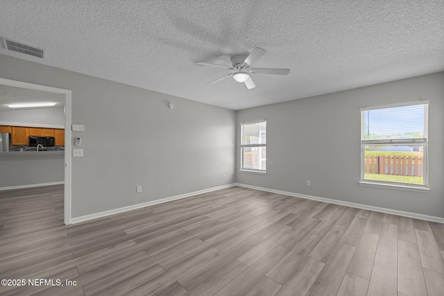 empty room featuring ceiling fan, a textured ceiling, wood finished floors, visible vents, and baseboards