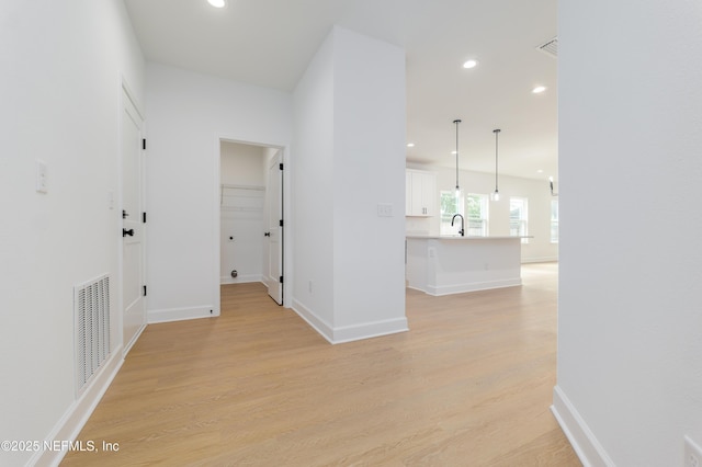 corridor with light wood-type flooring, a sink, visible vents, and recessed lighting