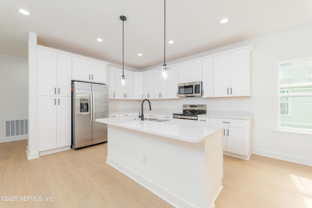 kitchen with stainless steel appliances, light countertops, visible vents, a sink, and light wood-type flooring