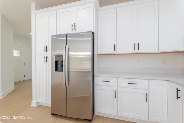 kitchen with light countertops, light wood-style flooring, stainless steel fridge with ice dispenser, and white cabinetry