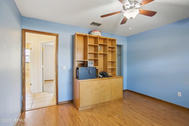 unfurnished office with ceiling fan, a textured ceiling, visible vents, baseboards, and light wood finished floors