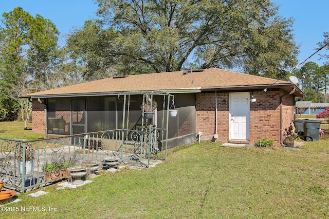 back of house with a shingled roof, a sunroom, brick siding, and a lawn