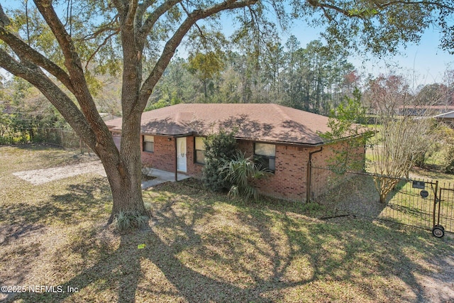 ranch-style home with a front yard, brick siding, fence, and roof with shingles