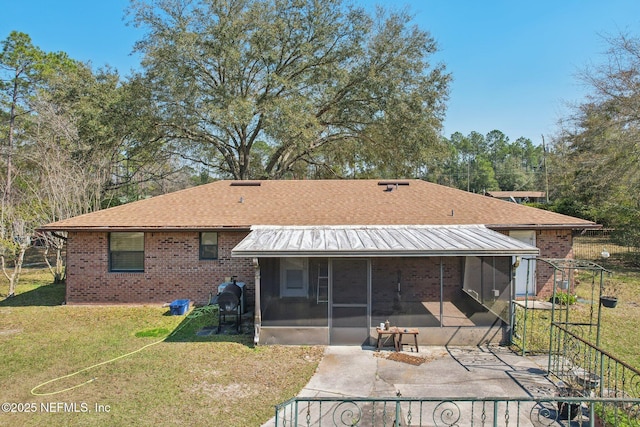 rear view of property with brick siding, a sunroom, a yard, roof with shingles, and a patio area