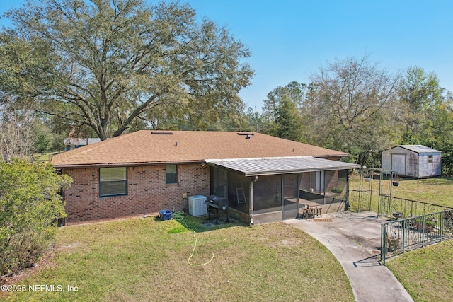 rear view of house with a storage shed, a lawn, a sunroom, central AC, and brick siding