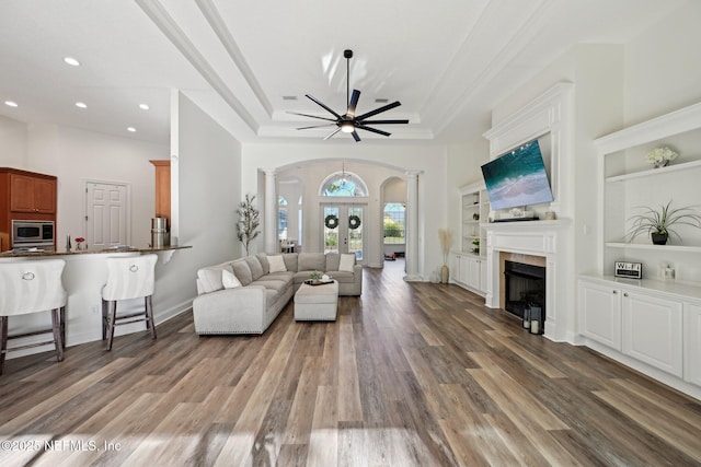 living area with decorative columns, arched walkways, wood finished floors, french doors, and a fireplace