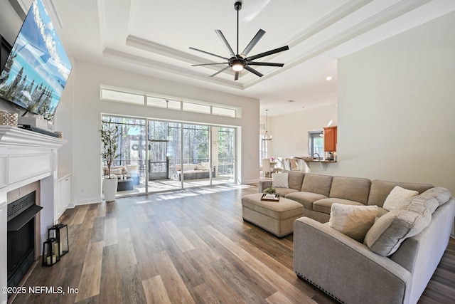 living room with a fireplace, a ceiling fan, a raised ceiling, and wood finished floors