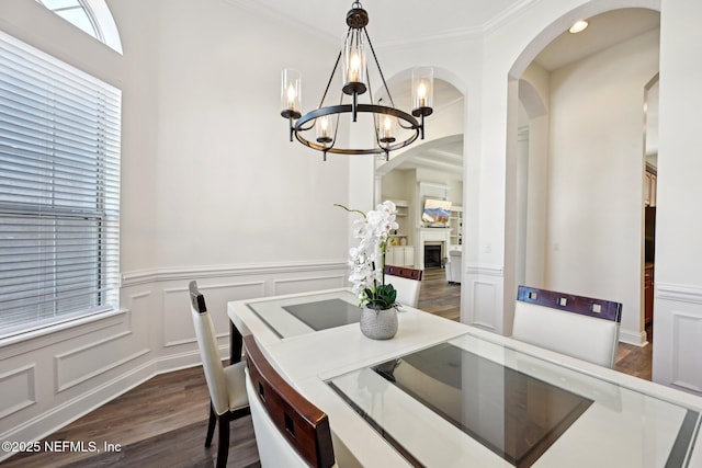 dining room with dark wood-style floors, crown molding, a fireplace, a chandelier, and a decorative wall