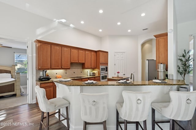 kitchen with a breakfast bar area, appliances with stainless steel finishes, dark stone countertops, a peninsula, and backsplash