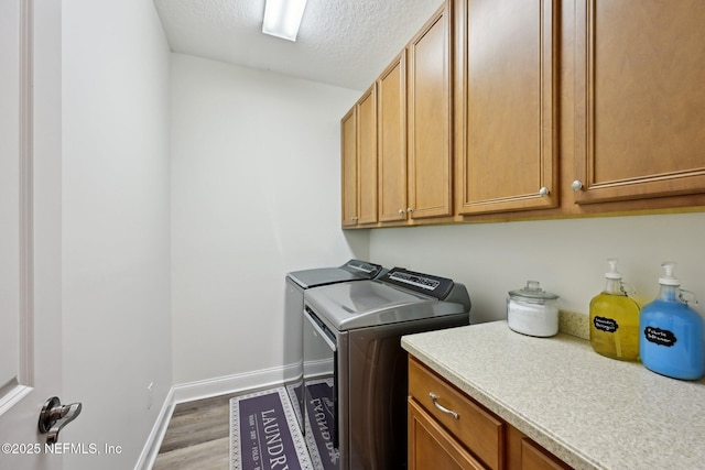 clothes washing area with washing machine and clothes dryer, cabinet space, a textured ceiling, wood finished floors, and baseboards