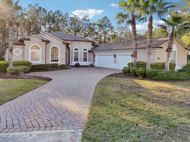 mediterranean / spanish-style house with an attached garage, a front yard, decorative driveway, and stucco siding