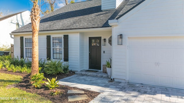 property entrance featuring an attached garage, a chimney, and roof with shingles