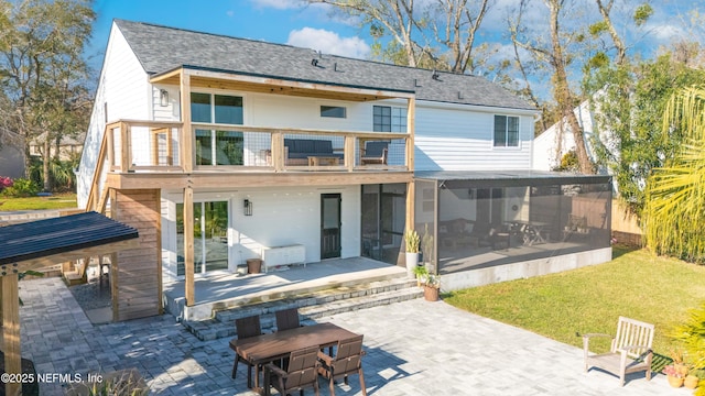 rear view of property with a sunroom, roof with shingles, a patio, and a lawn