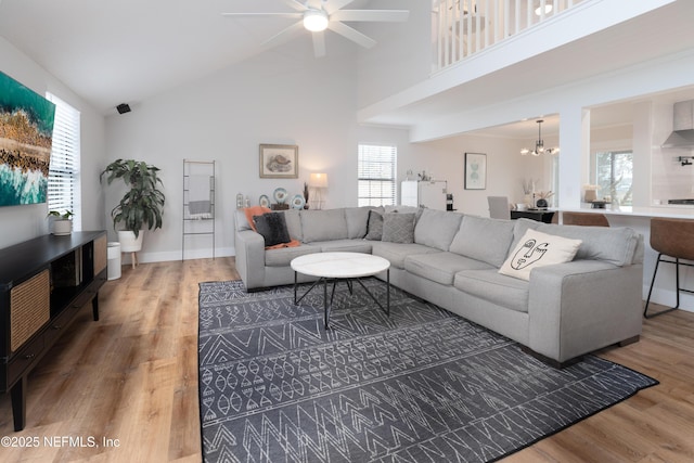 living area with high vaulted ceiling, a wealth of natural light, a notable chandelier, and wood finished floors