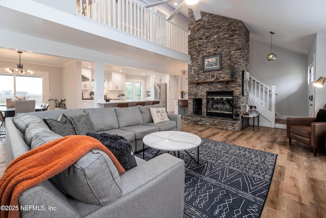 living room featuring ceiling fan with notable chandelier, a wealth of natural light, a fireplace, and wood finished floors