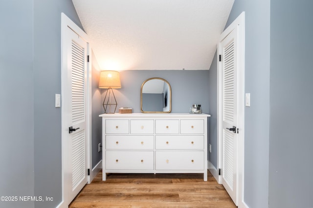 unfurnished bedroom with baseboards, a textured ceiling, lofted ceiling, and light wood-style floors