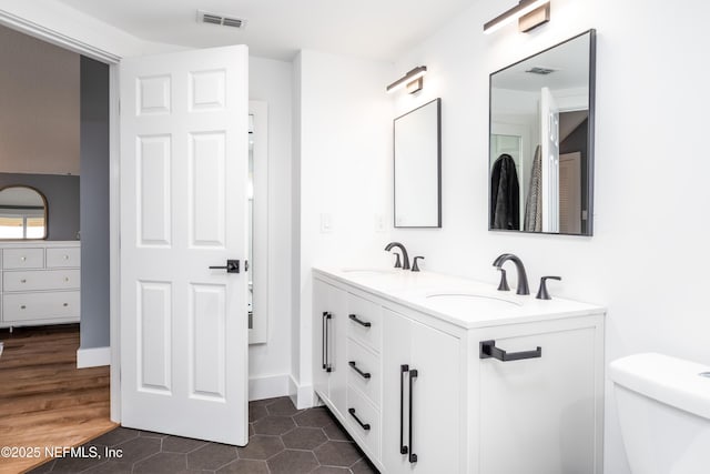 bathroom featuring double vanity, visible vents, toilet, and a sink