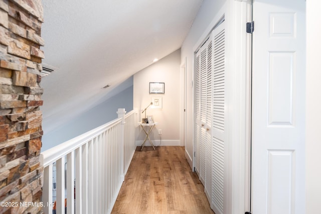 corridor featuring vaulted ceiling, an upstairs landing, light wood-style flooring, and baseboards