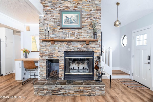 living area with crown molding, a stone fireplace, baseboards, and wood finished floors