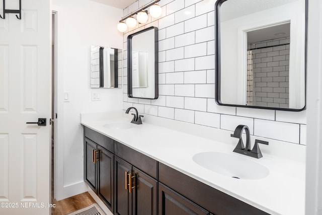 bathroom featuring wood finished floors, a sink, decorative backsplash, and double vanity