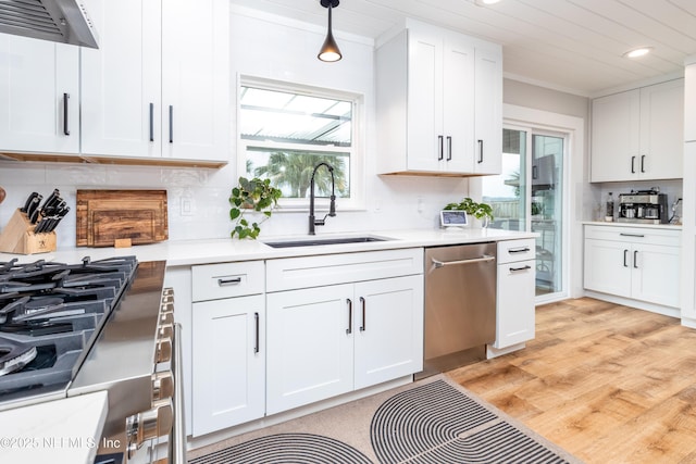 kitchen featuring hanging light fixtures, stainless steel dishwasher, wall chimney range hood, and white cabinets