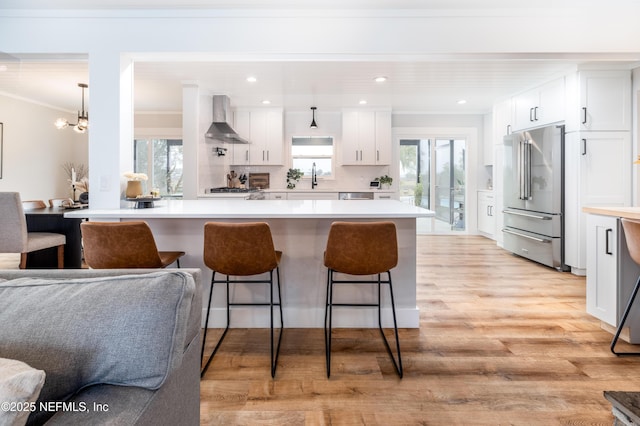 kitchen featuring wall chimney exhaust hood, high quality fridge, white cabinetry, and light countertops