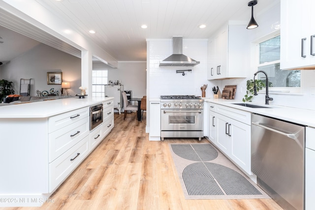 kitchen with pendant lighting, light countertops, appliances with stainless steel finishes, white cabinets, and wall chimney range hood