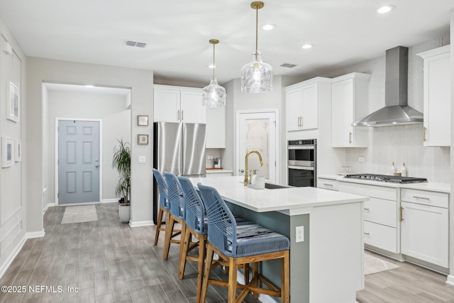 kitchen with a sink, visible vents, light countertops, wall chimney range hood, and a center island with sink