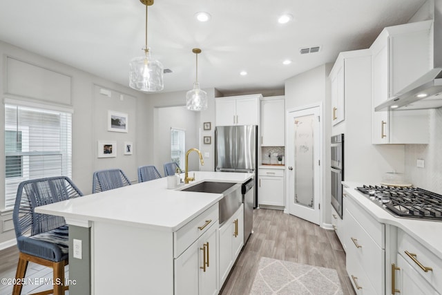 kitchen featuring a breakfast bar area, light countertops, visible vents, a kitchen island with sink, and wall chimney exhaust hood