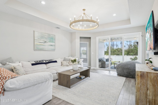 living area featuring a notable chandelier, a tray ceiling, wood finished floors, and recessed lighting