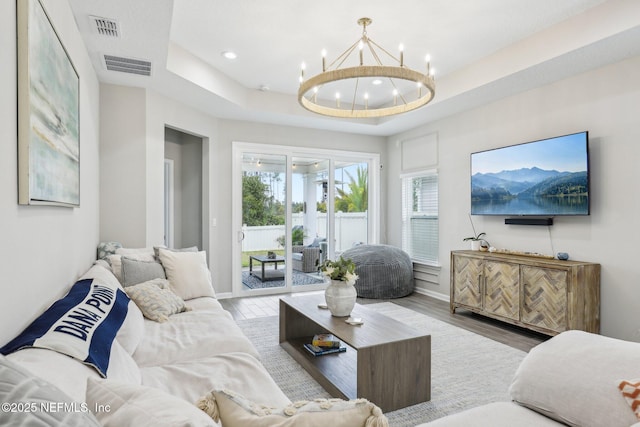 living area featuring light wood-type flooring, a raised ceiling, and visible vents