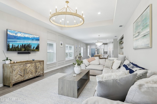 living area featuring visible vents, a raised ceiling, wood finished floors, an inviting chandelier, and recessed lighting