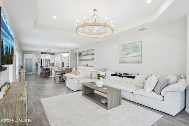 living room featuring visible vents, a raised ceiling, wood finished floors, a notable chandelier, and recessed lighting