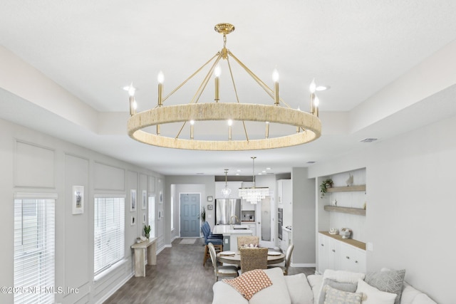 living room featuring a tray ceiling, visible vents, an inviting chandelier, wood finished floors, and baseboards