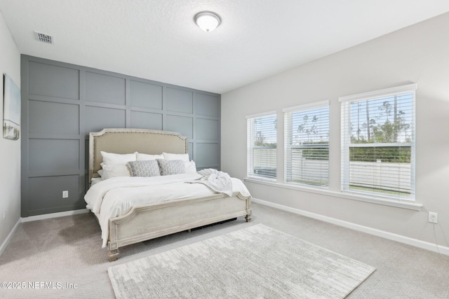 bedroom with light colored carpet, visible vents, a decorative wall, and baseboards