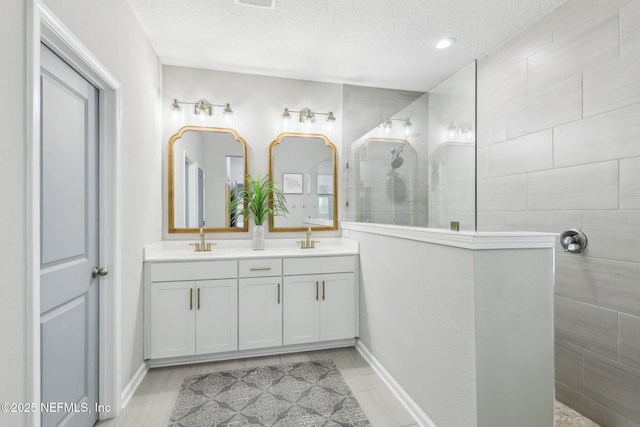 bathroom with double vanity, a textured ceiling, a walk in shower, and a sink