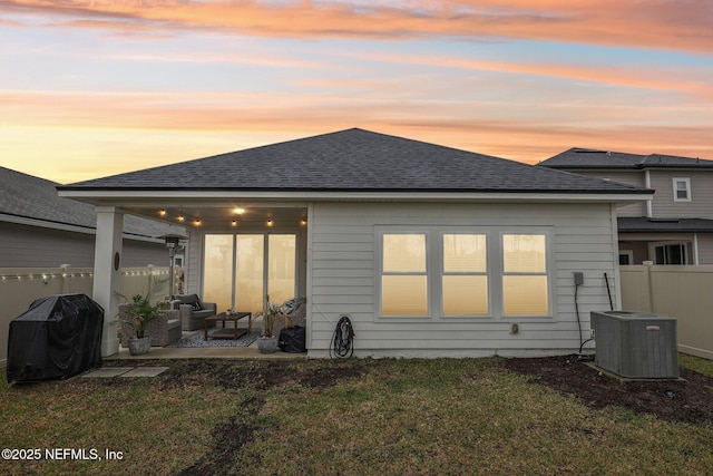 back of property with a shingled roof, cooling unit, fence, and a lawn