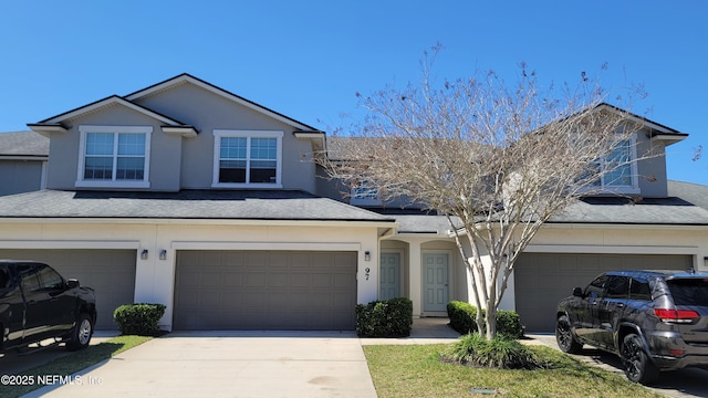 traditional-style house with a garage, concrete driveway, a shingled roof, and stucco siding