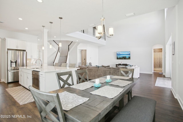 dining space with baseboards, dark wood finished floors, arched walkways, stairway, and an inviting chandelier