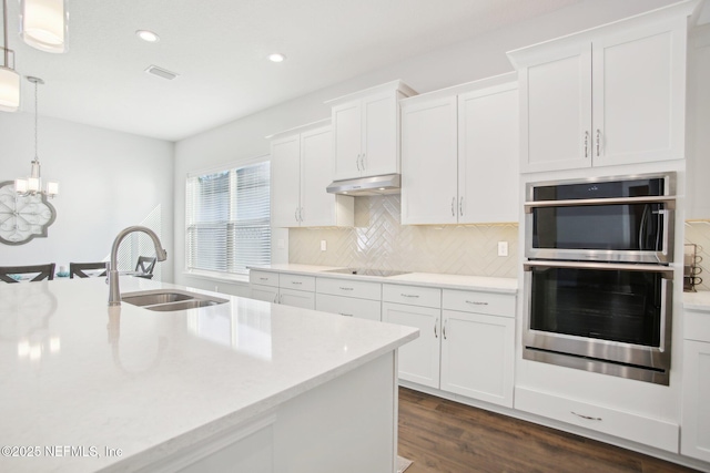 kitchen with black electric stovetop, under cabinet range hood, a sink, white cabinetry, and backsplash