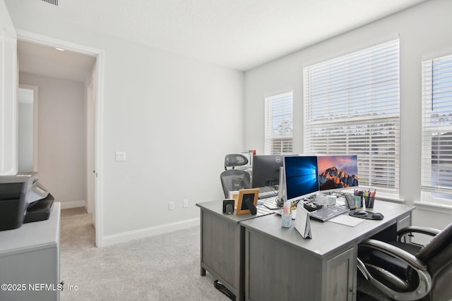 office space with baseboards, plenty of natural light, and light colored carpet