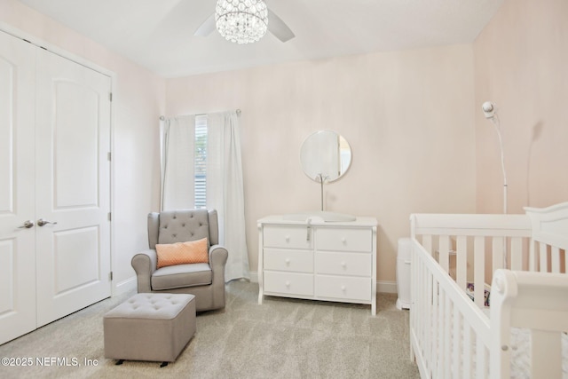 bedroom featuring a crib, baseboards, a ceiling fan, and light colored carpet