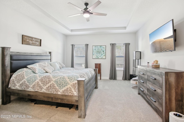 bedroom featuring a ceiling fan, a tray ceiling, light carpet, and baseboards